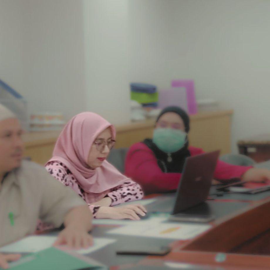 Ariantika reviewing paperwork at a shared desk with two colleagues during a research meeting in an office